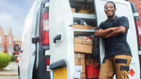 A tradesman stood at the side of his van with his arms folded smiling to camera on a housing estate