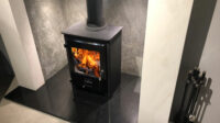 Image of square cast iron woodburner on top of granite slab with orange fire flames burning.