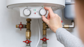 Hand puts thermostat of electric water heater (boiler) in economy mode. 