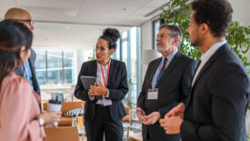 Diverse group of male and female business professionals talking together in corporate office lobby during social gathering.