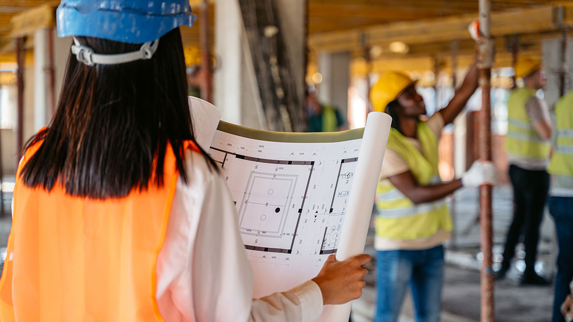 Female architect looking at the construction plan on a construction site (building interior).