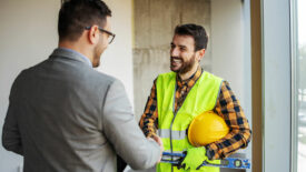 Smiling construction worker shaking hands with supervisor while standing in building in construction process.