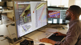 African American / Afro-Caribbean male working with large computer screens and CAD. He’s designing built in insulation structures in domestic homes.