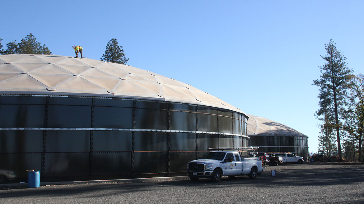 White trucks parked in front of two large dome buildings, a man working on top of the domed roof.