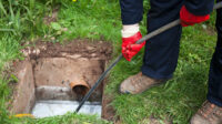 Drain being cleared by worker in navy overalls.