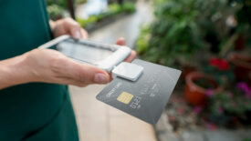 Close up of saleswoman doing the checkout using a credit card reader and smartphone at a garden center. **DESIGN ON CREDIT CARD WAS MADE FROM SCRATCH BY US**