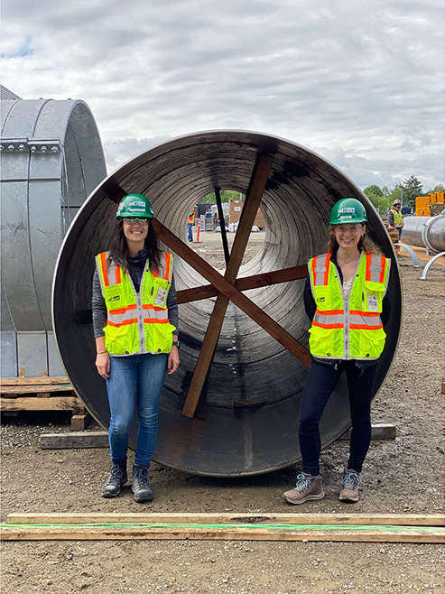 Two female JH Kelly employees posing in front of a large tube.