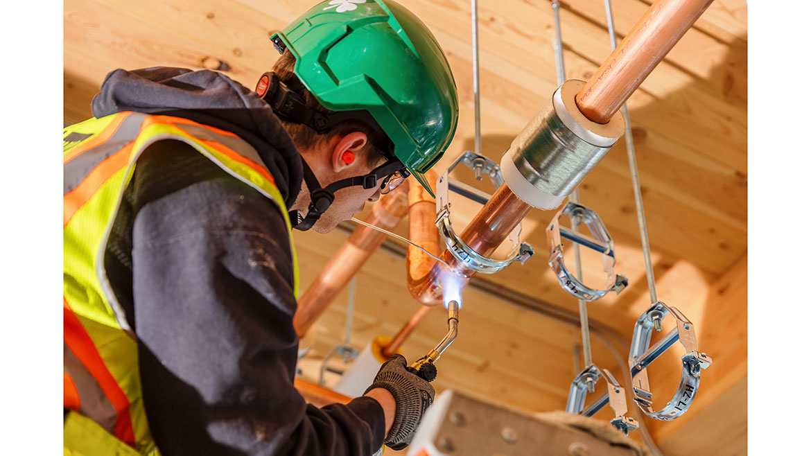 A JH Kelly plumber solders copper piping at a confidential client location.