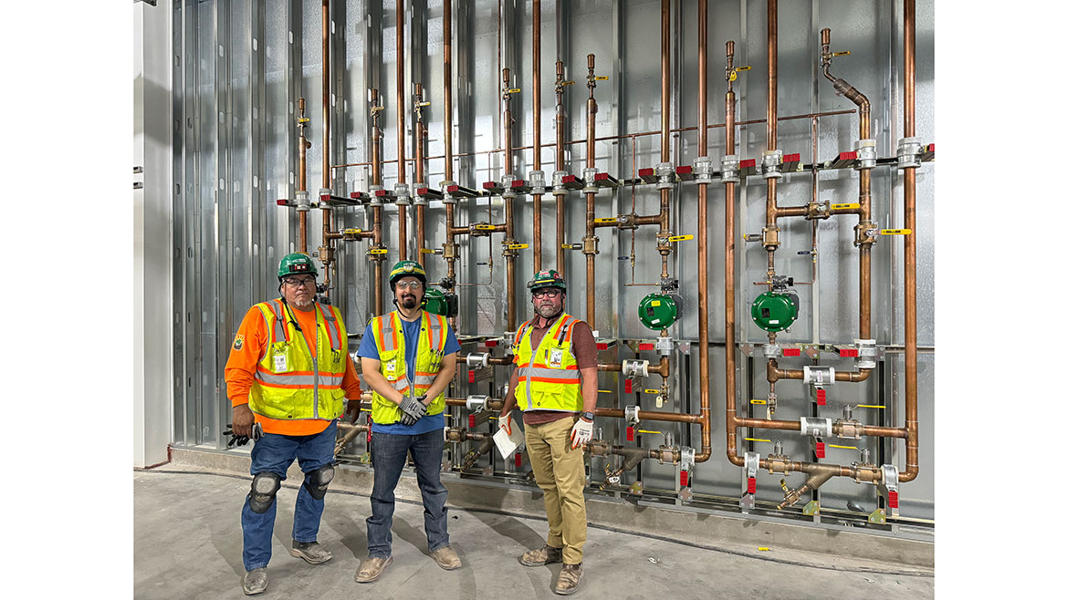 JH Kelly's Craft leadership poses in front of some freshly installed copper piping at a confidential client location.