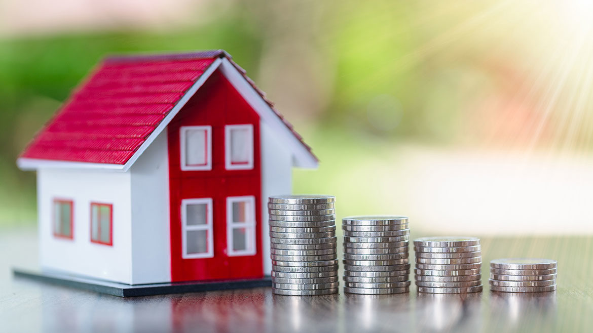 Four stacks of silver coins next to a red and white toy house with a blurry background.