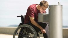 Man in a wheelchair drinking water from a faucet.