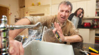 Man has a plumbing mishap with the kitchen sink as water gushes from the broken tap.