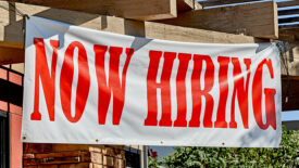 Now Hiring sign hanging outside a building.