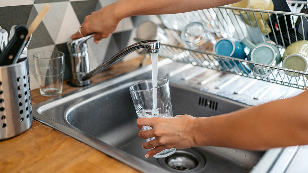 Young woman filling a glass of water in the sink. Close-up.